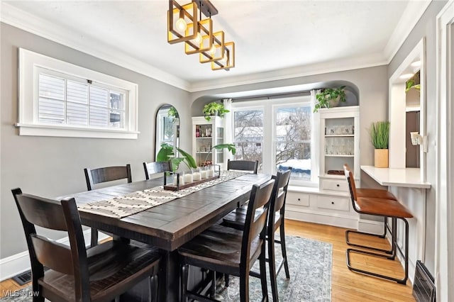 dining space with arched walkways, crown molding, light wood finished floors, visible vents, and baseboards