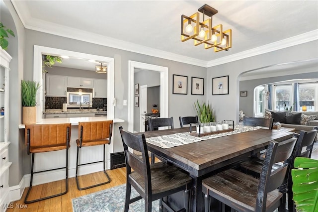 dining area featuring ornamental molding, light wood-type flooring, arched walkways, and an inviting chandelier