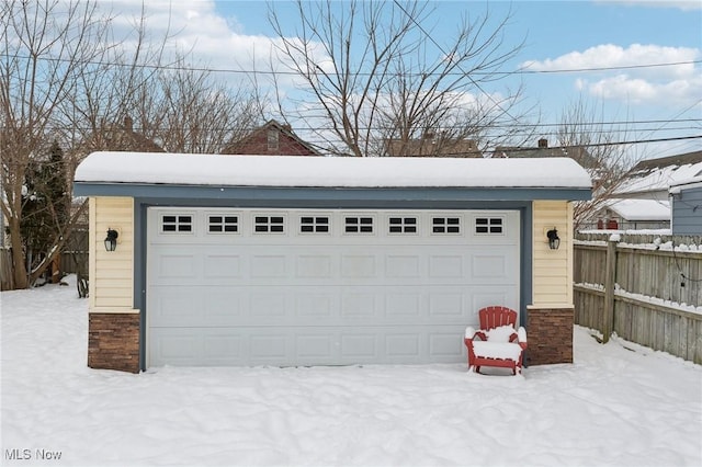 snow covered garage featuring a garage and fence