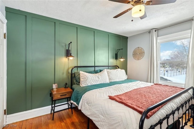 bedroom featuring dark wood-style floors, a decorative wall, a textured ceiling, and ceiling fan