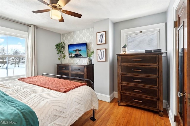 bedroom featuring an accent wall, a ceiling fan, baseboards, light wood-style floors, and wallpapered walls