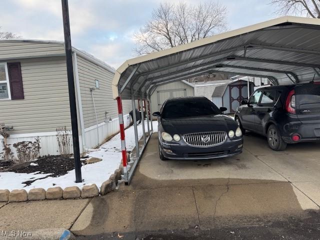 snow covered parking with a carport and a shed