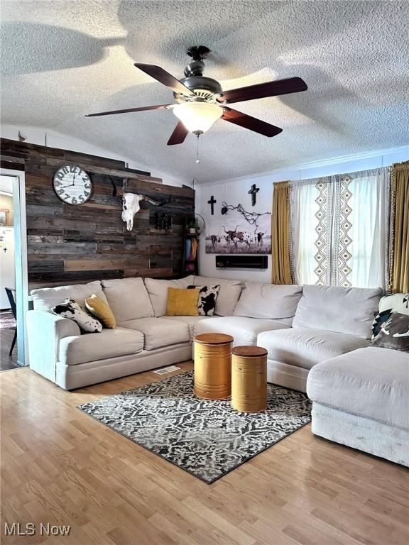 living area with a textured ceiling, ceiling fan, wood finished floors, and wooden walls