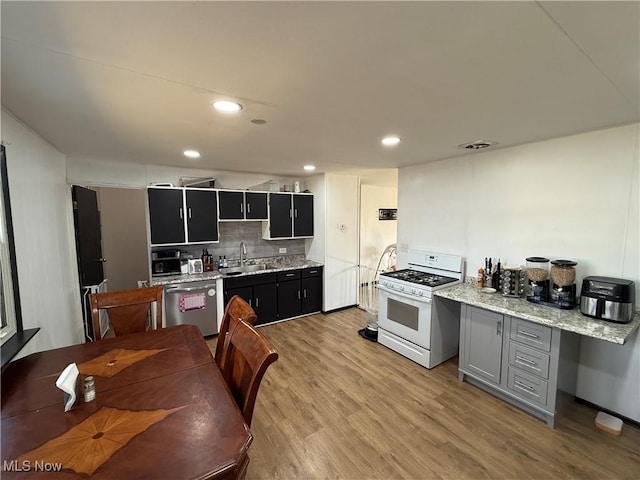 kitchen with light wood-style flooring, backsplash, white gas stove, stainless steel dishwasher, and a sink