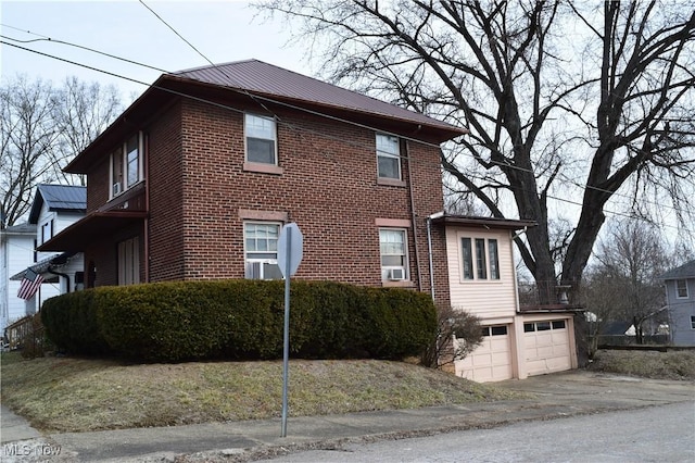 view of property exterior featuring metal roof, brick siding, an attached garage, and driveway