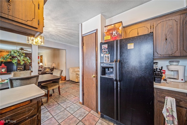 kitchen featuring brown cabinetry, light countertops, black fridge with ice dispenser, and a textured ceiling