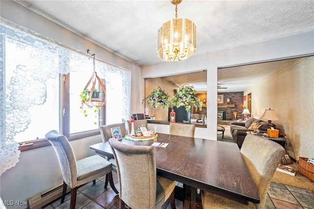 dining room with a textured ceiling, a notable chandelier, a large fireplace, baseboard heating, and stone tile flooring