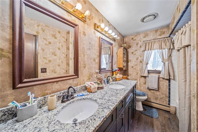 bathroom featuring a baseboard heating unit, wood finished floors, a sink, and toilet