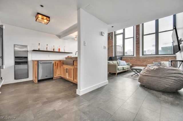 kitchen with brick wall, a sink, baseboards, open floor plan, and stainless steel dishwasher