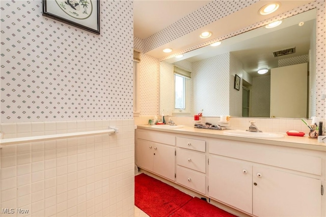 full bathroom featuring wallpapered walls, tile walls, a sink, and a wainscoted wall