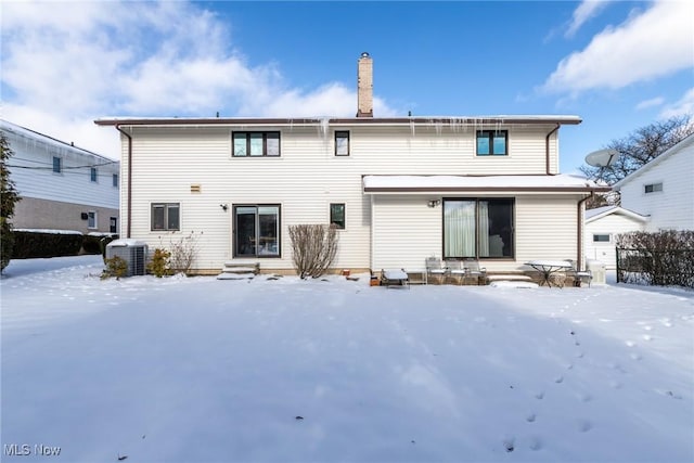 snow covered house with entry steps, a chimney, and central air condition unit