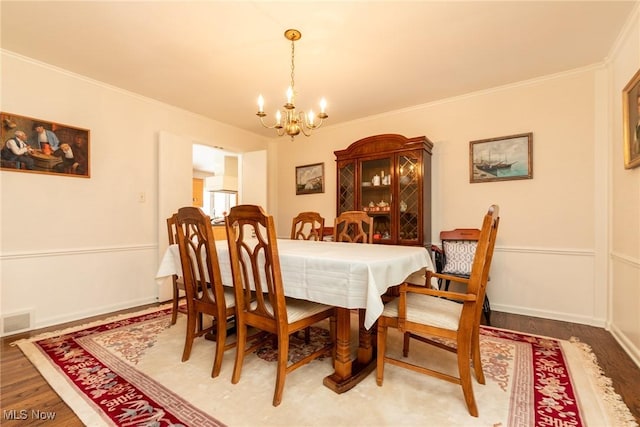 dining space with a notable chandelier, visible vents, wood finished floors, and ornamental molding