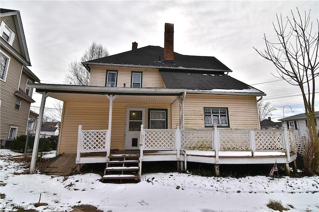 snow covered house featuring covered porch and a chimney