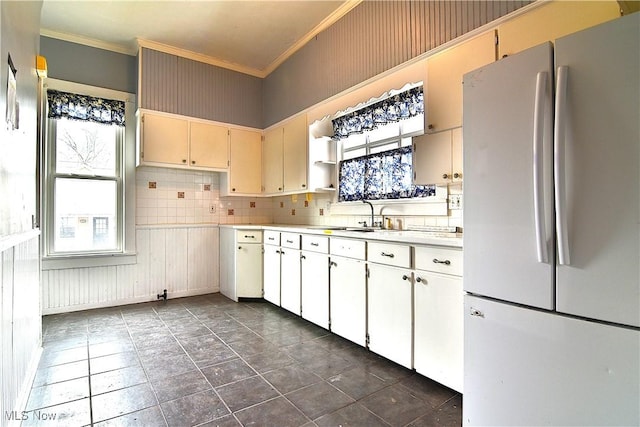 kitchen featuring light countertops, ornamental molding, freestanding refrigerator, a sink, and plenty of natural light