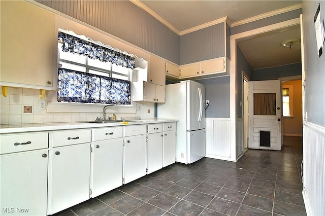 kitchen with light countertops, freestanding refrigerator, wainscoting, a sink, and white cabinetry