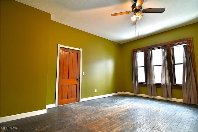 spare room featuring ceiling fan, dark wood-style flooring, and baseboards