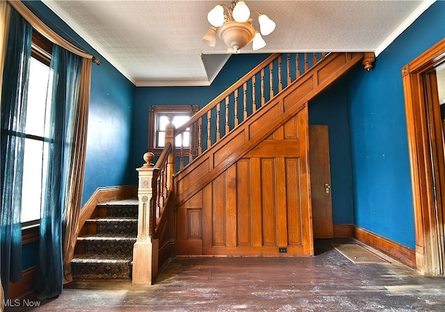 stairway with a notable chandelier, crown molding, a textured ceiling, wood finished floors, and baseboards