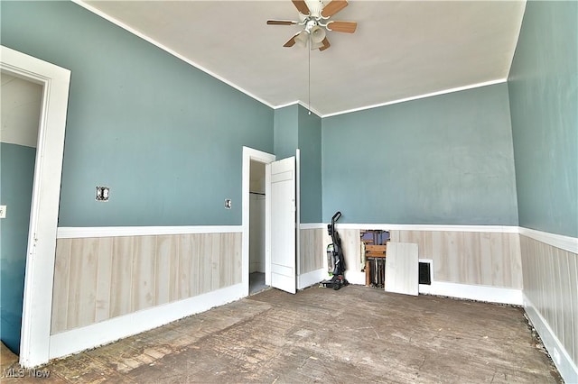 unfurnished room with crown molding, wainscoting, ceiling fan, and wooden walls