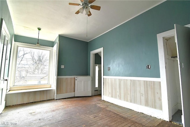 spare room with a wainscoted wall, wood finished floors, a ceiling fan, and crown molding