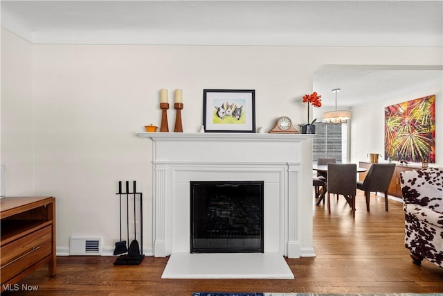 details featuring a fireplace with raised hearth, a notable chandelier, wood finished floors, visible vents, and baseboards