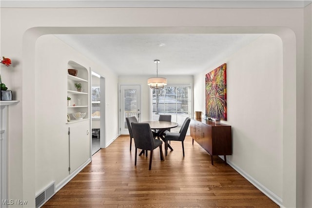 dining area featuring built in shelves, visible vents, baseboards, and wood finished floors