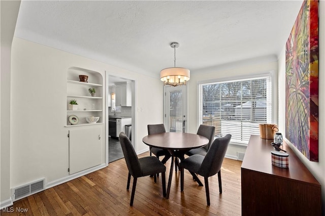 dining area with built in features, visible vents, an inviting chandelier, a textured ceiling, and wood finished floors