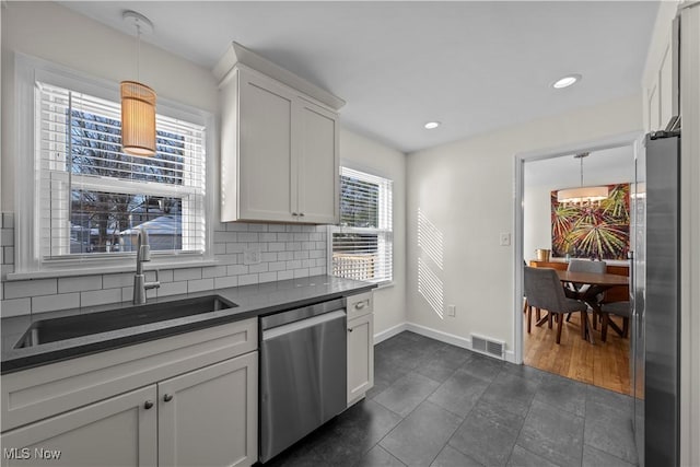 kitchen with dark countertops, hanging light fixtures, stainless steel appliances, white cabinetry, and a sink