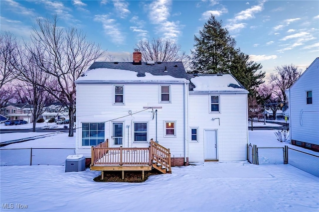 snow covered house with a chimney, fence, and a wooden deck