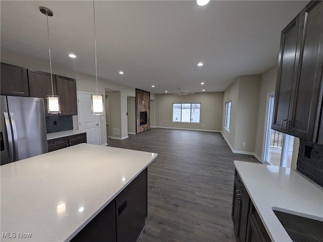 kitchen with dark wood finished floors, open floor plan, stainless steel fridge, and hanging light fixtures