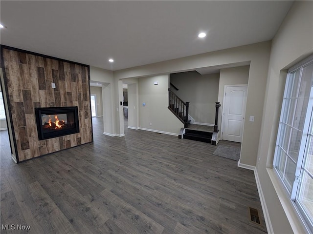 unfurnished living room with dark wood-type flooring, baseboards, a tiled fireplace, and stairs