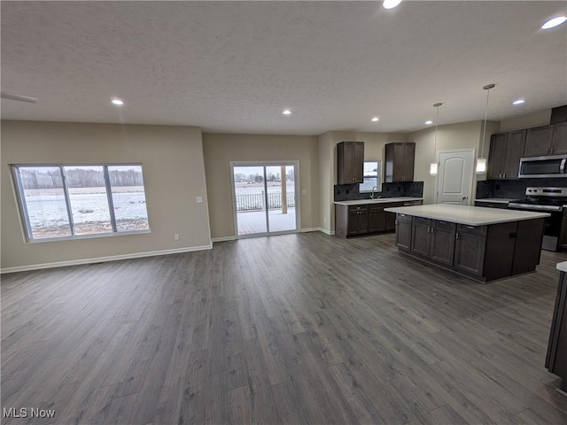 kitchen with stainless steel appliances, light countertops, hanging light fixtures, open floor plan, and a kitchen island