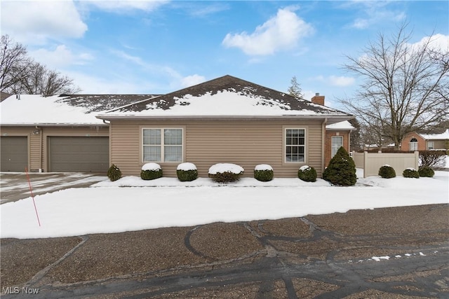 snow covered property featuring driveway, a chimney, an attached garage, and fence