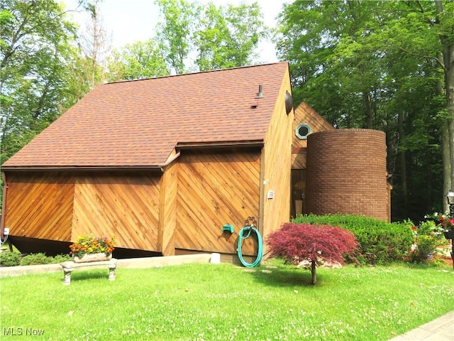 exterior space with a shingled roof, a lawn, and a garage