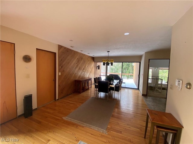 dining area featuring light wood-style floors, an accent wall, a chandelier, and wood walls