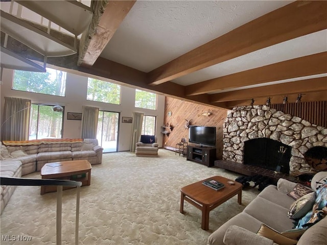 living area with a textured ceiling, a stone fireplace, wooden walls, carpet floors, and beam ceiling