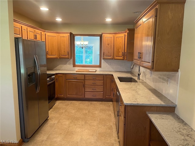 kitchen with appliances with stainless steel finishes, brown cabinetry, a sink, and light stone countertops