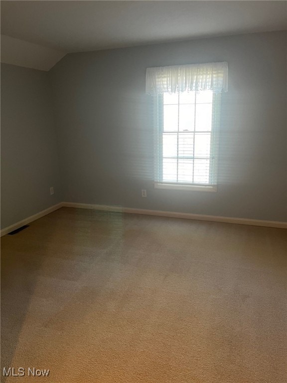 spare room with carpet, visible vents, lofted ceiling, and baseboards