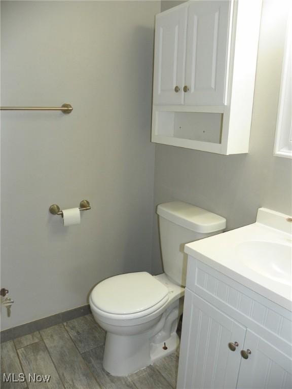 bathroom with toilet, baseboards, wood finish floors, and vanity