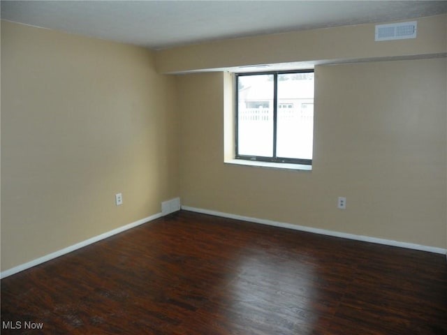 spare room with dark wood-style floors, visible vents, and baseboards