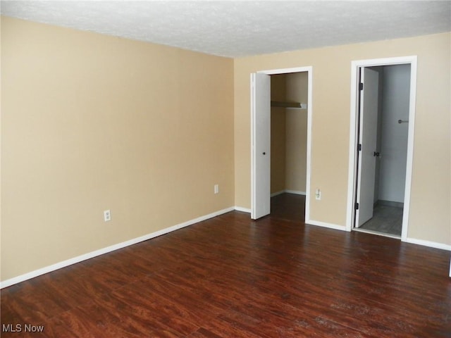 unfurnished bedroom with a spacious closet, dark wood-type flooring, and baseboards