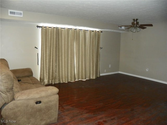 living area with a textured ceiling, ceiling fan, dark wood-style flooring, visible vents, and baseboards