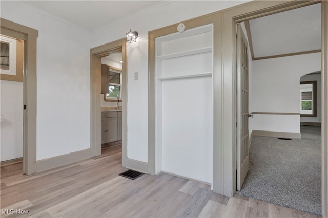 interior space featuring arched walkways, light wood-style floors, visible vents, and crown molding