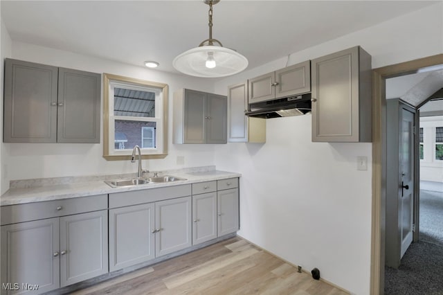 kitchen featuring decorative light fixtures, light countertops, gray cabinetry, a sink, and under cabinet range hood