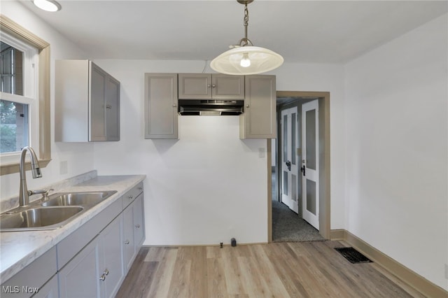 kitchen with pendant lighting, light countertops, gray cabinetry, a sink, and under cabinet range hood