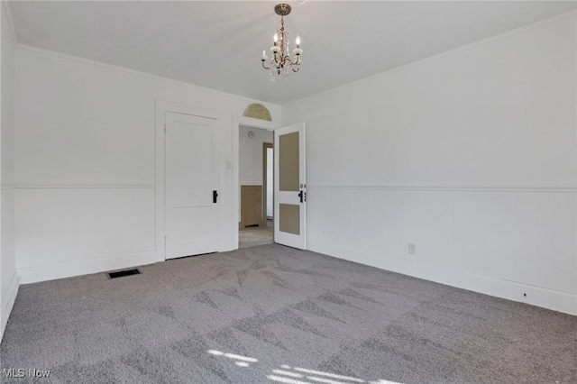 carpeted empty room featuring a wainscoted wall, visible vents, a chandelier, and crown molding