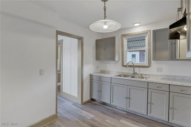 kitchen with light wood-style floors, a sink, hanging light fixtures, and gray cabinetry