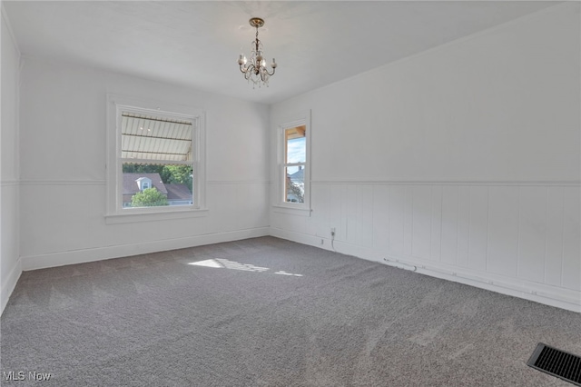 carpeted spare room featuring a chandelier, a wainscoted wall, and visible vents