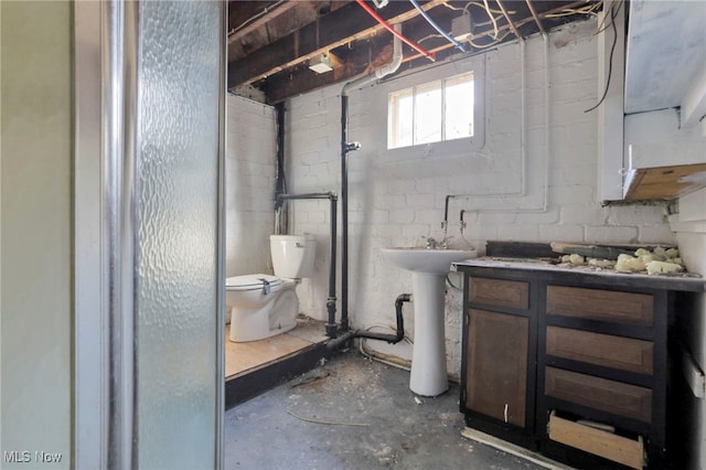 full bathroom featuring concrete block wall, a sink, toilet, and unfinished concrete floors