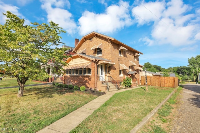 view of front of property with brick siding, a chimney, a front lawn, and fence