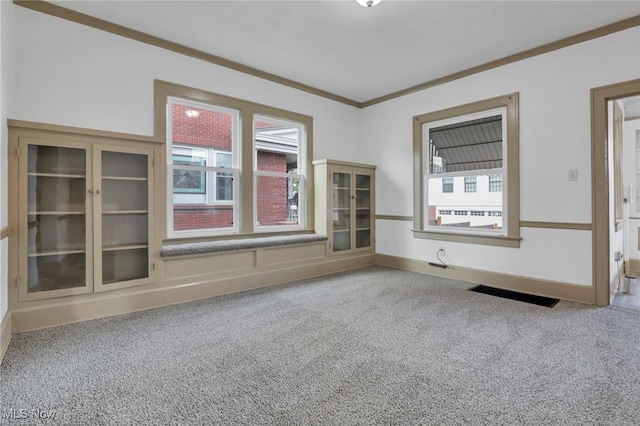 unfurnished room with carpet floors, ornamental molding, plenty of natural light, and visible vents